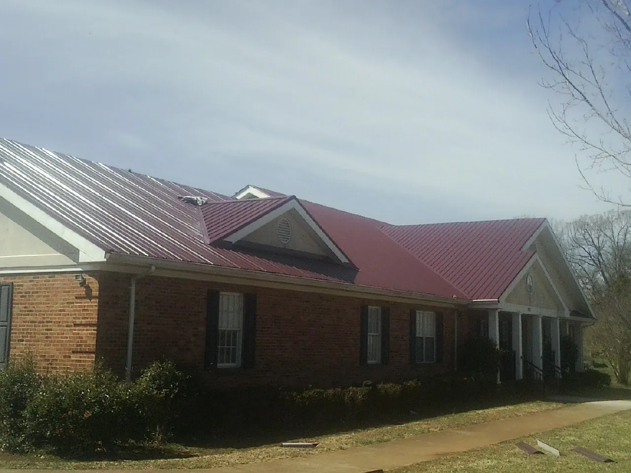 Red metal roof with gabled entries on a long brick building, from a Hail Damage Roof Repair job in Boulder